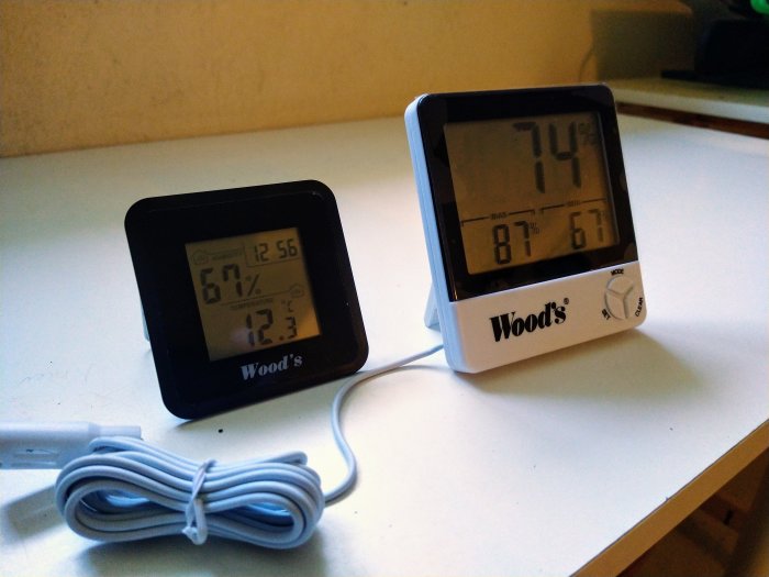 Två Wood's hygrometrar visar olika luftfuktighet och temperatur på en vit yta.