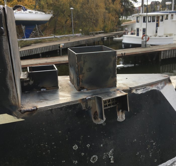 Svetsade takgenomföringar för skorstenar på en båt, med en bakgrund av marina fordon.