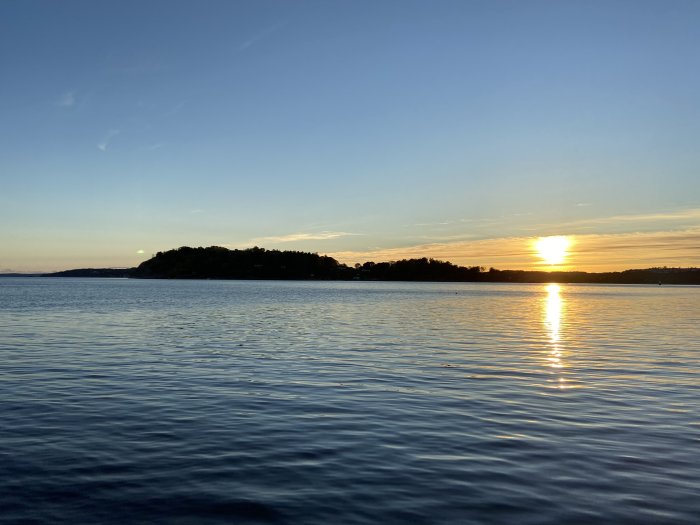 Solnedgång över havet med silhuett av en ö och reflektioner i vattnet.