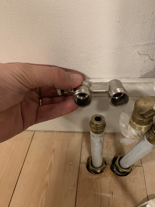 Hand håller en 22mm förbikopplingsrör bredvid 20mm rör som kommer från golvet vid radiatorinstallation.