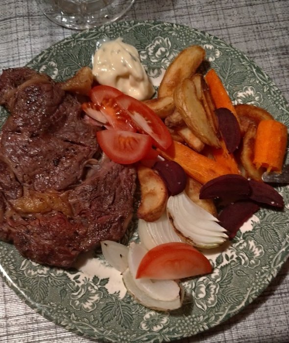 Grillad entrecote på tallrik med klyftpotatis, morotsstavar, lök och tomat, serverad med bearnaisesås.