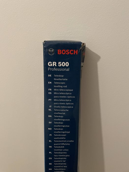 Förpackning av Bosch GR 500 teleskopisk nivelleringsstång lutad mot en vit vägg.