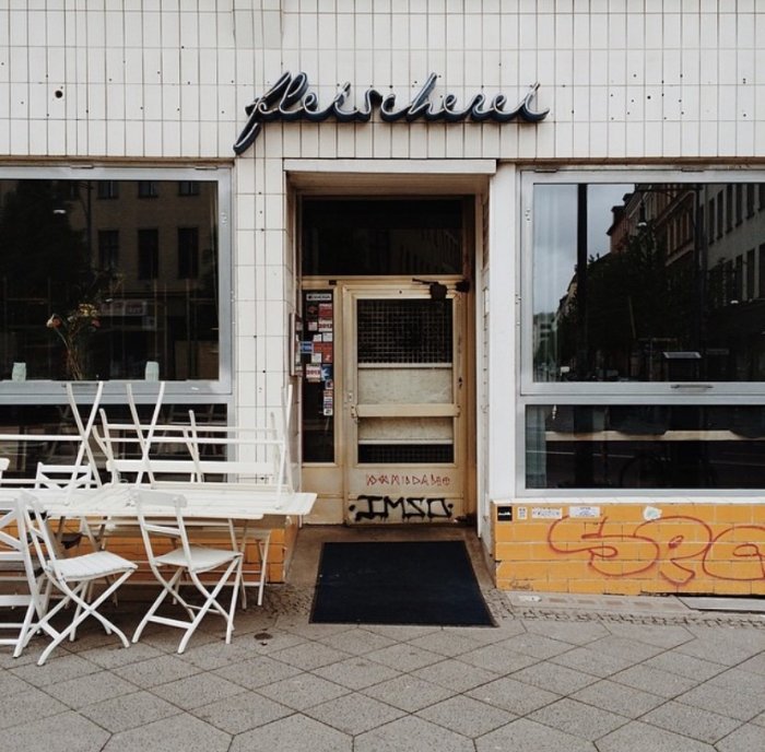 Bistroentré med kaklad front och centralt placerade kapade plattor, skylt ovanför och uteservering.