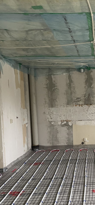 Rör i kökshörn med synligt dagvattenrör och golvvärmeinstallation före renovering.