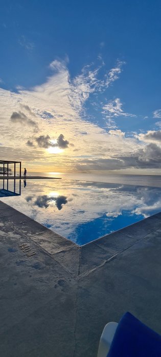 Solnedgång med moln reflekterad i ett lugnt vatten, som skapar en illusion av en dubbel himmel.