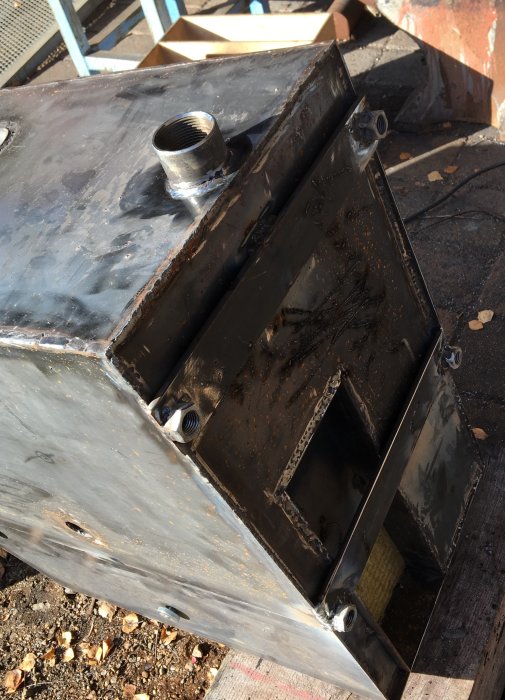 Svetsade delar på en kamin med röranslutning och förstärkta plåtdelar i en verkstadsmiljö.