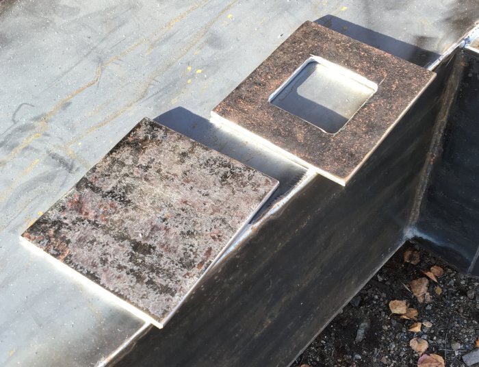 Svetsade metallplåtar och fartygsplåt förberedda för kaminrenovering, med en urklippt kvadrat och patina.