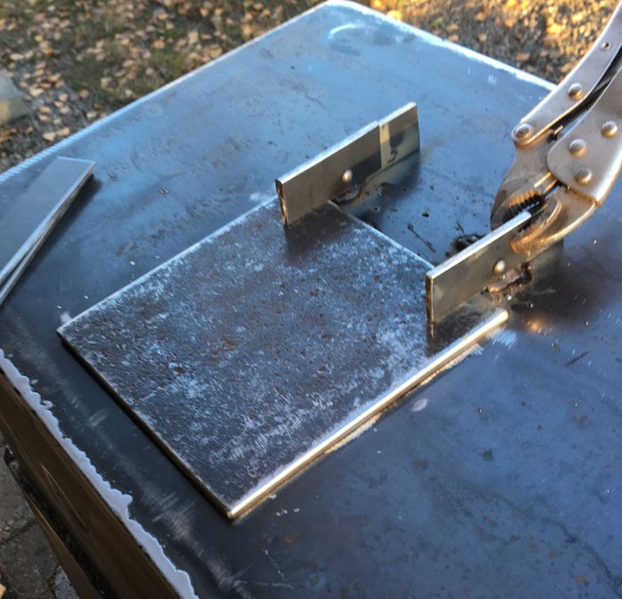 Metalldel med grov struktur fastklämd med tvingar för borrning vid kaminrenovering.
