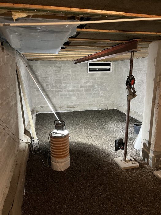Ett källarrum under renovering med nyligen utlagt makadam, en lampa och en lång rätskiva.