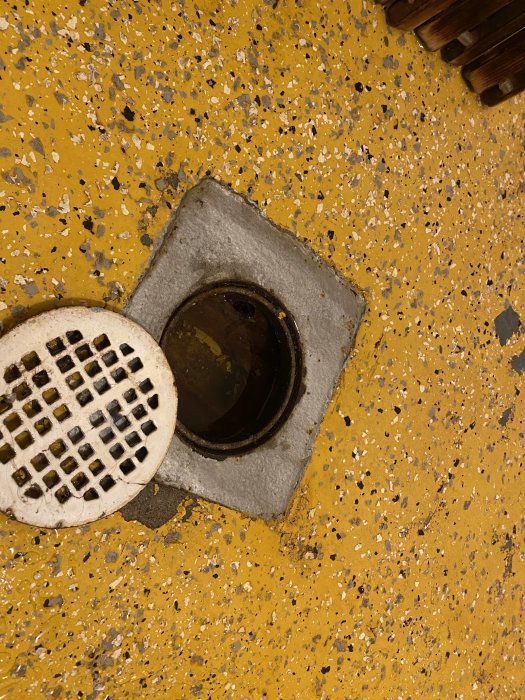 Gammal rostangripen golvbrunn med lyft bort golvrist på ett gulmålat betonggolv.
