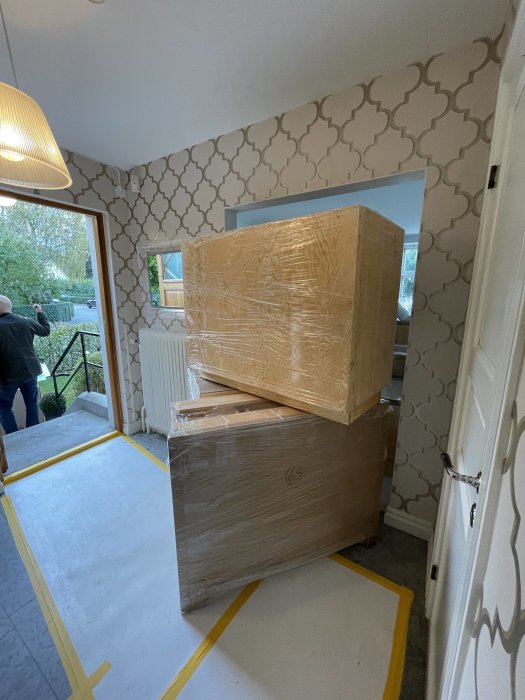 Inpackade köksdelar placerade i renoverat rum med skydd på golvet, väntar på installation.