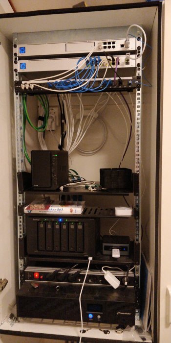 Nätverksrack i garderob med router, switch, patchpanel, NAS-enheter, gateway, NUC och UPS.