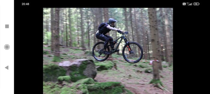 Cyklist i hjälm utför hopp på mountainbike i skogsområde, downhill-stil.