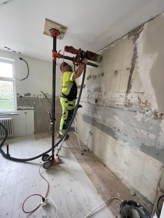 Arbetare i skyddskläder använder en diamantborr för att göra hål i en betongvägg i ett renoveringsprojekt.