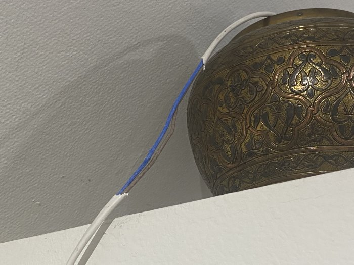 Elkabel med avskalat yttre, nära dekorativ taklampa, efter att ha blivit tuggad av papegoja.