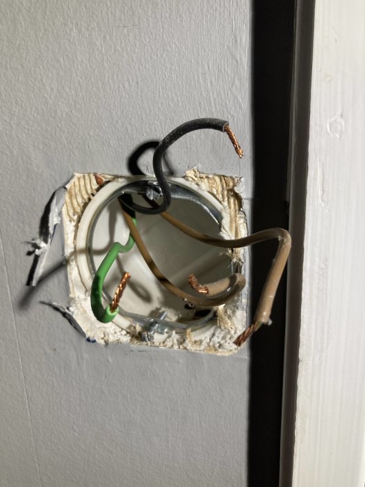 Eluttag med oskyddade elektriska ledningar och synliga anslutningar på en vägg.
