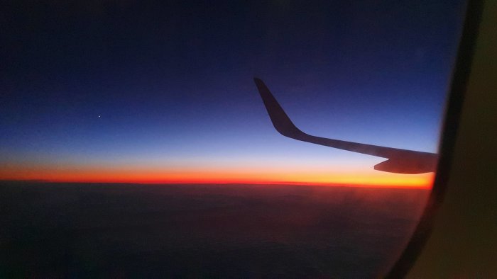 Flygplansvinge mot en färgrik solnedgångshimmel sett från flygplansfönster.