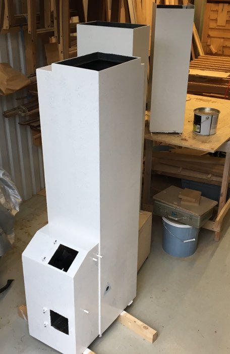 Nygrundad kamin i en verkstad med burkar av målarfärg och träplankor.