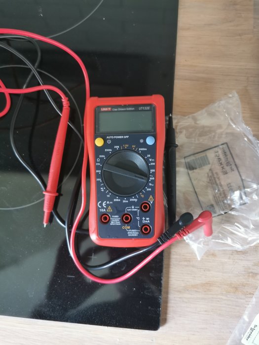 Digital multimeter med röda och svarta mätprober på ett svart underlag.