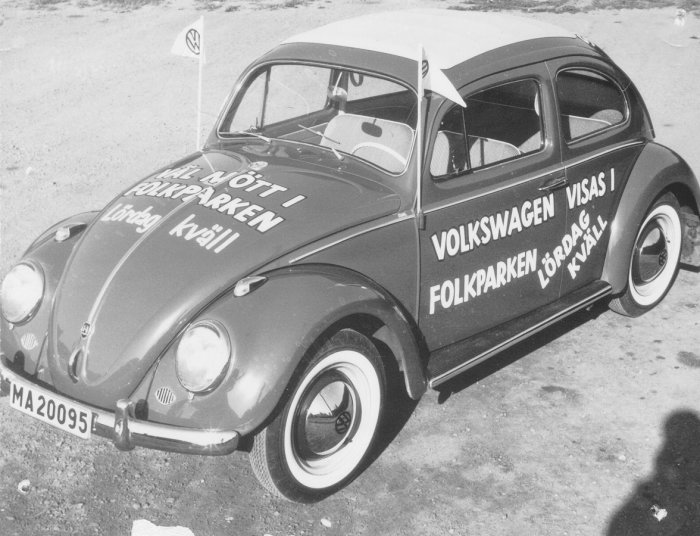 Svart Volkswagen Typ 1 med texten "Kom Väl" och reklam för event i Folkparken.