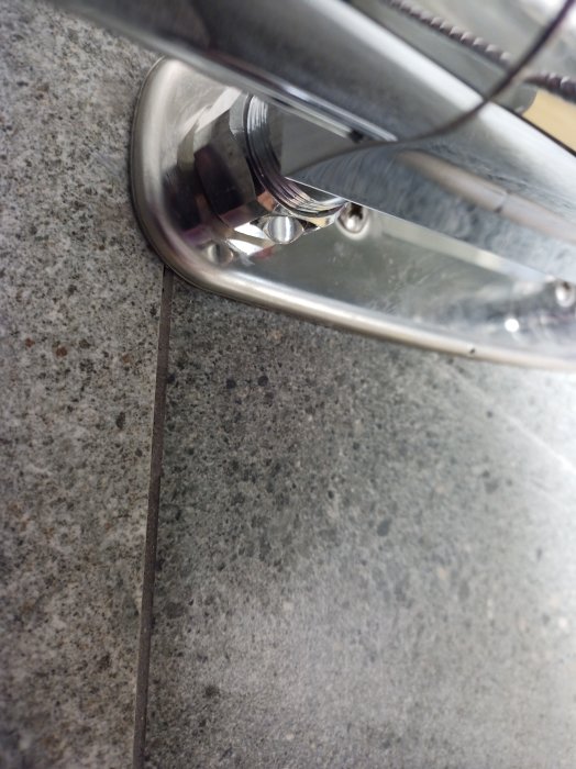 Vatten droppar vid ett kromat blandarfäste på granitbänk, tecken på läckage.