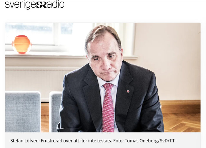 Man i kostym med bekymrad min, sitter vid ett bord, inomhusmiljö.
