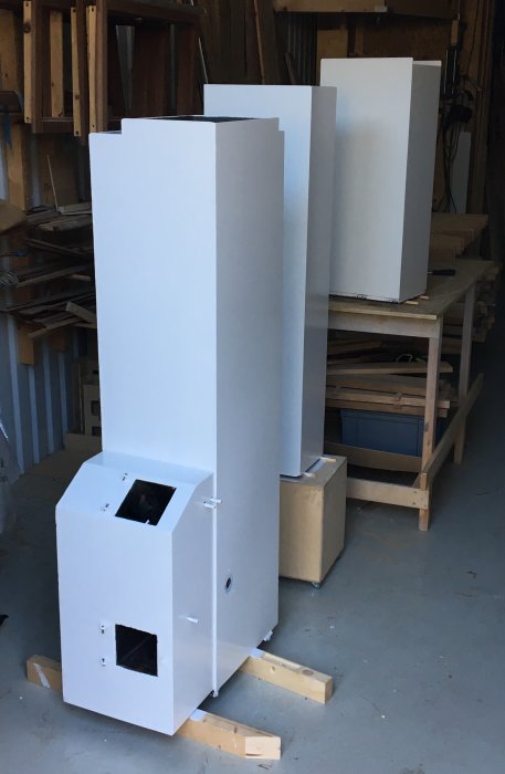 Nymålad kamin med slätstruken yta i en snickerilokal, står på träpallar mellan arbetsbord och materialhyllor.