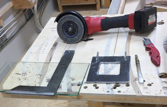 Ett 6mm lamellglas ligger på en arbetsbänk med ett stålreglage och verktyg inklusive en vinkelslip och glaskniv.