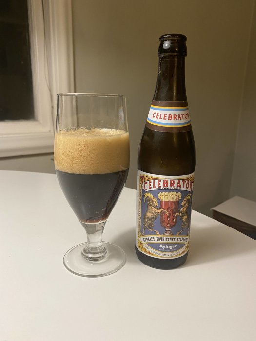 Mörkt tyskt öl i glas bredvid en flaskan Celebrator Doppelbock på ett vitt bord.