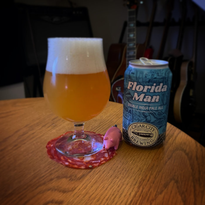 Ölglas fyllt med skummande öl på en bricka bredvid en burk "Florida Man Double India Pale Ale" och en figur.