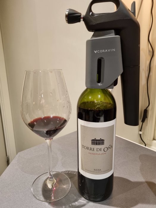 En flaska Rioja Torre de Oña Reserva 2014 med ett Coravin-system och ett halvfullt glas vin.