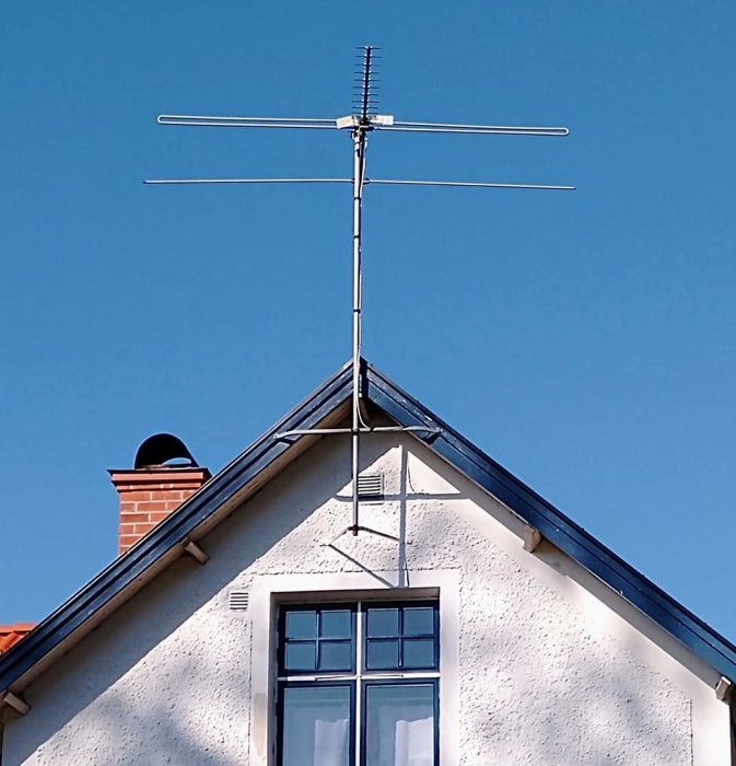 Gammal TV-antenn monterad på husets tak mot en klarblå himmel.