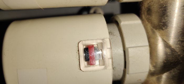 Elektromekaniskt styrdon till golvvärme med synlig röd indikator och svart tryckknapp.
