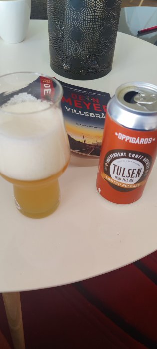 Ett glas öl bredvid en öppnad burk och en bok på ett vitt bord.
