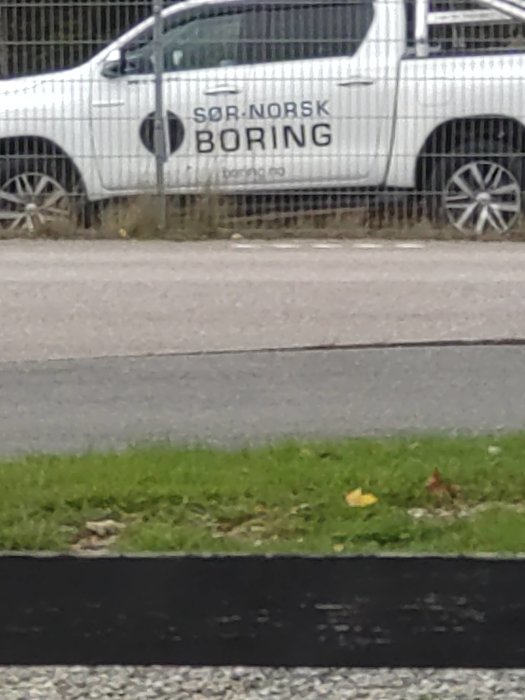 Vit bil med texten "SØR-NORSK BORING" på sidan parkerad vid vägkanten.