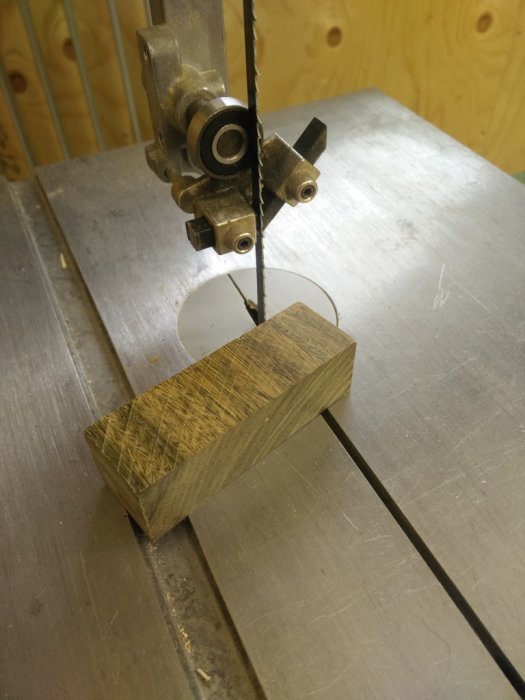 Bandsåg med ett kullager nära sågbladet som skär genom ett trästycke på arbetsbordet.