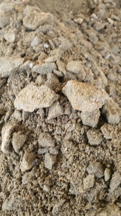 Närbild av upplyft marksten och grävd makadam vid en carport som förbereds för ombyggnad till garage.