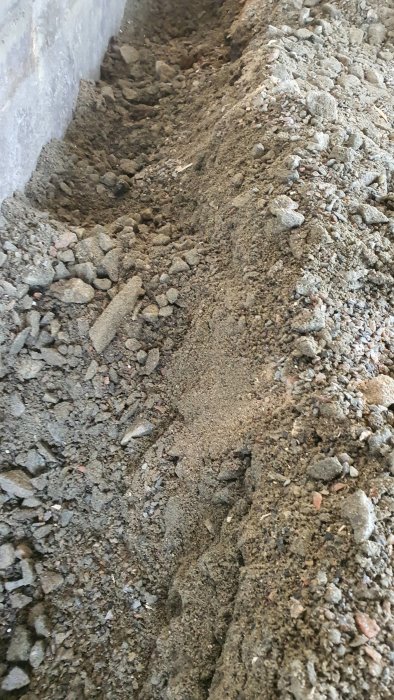 Grävd mark vid husgrund med synligt bärlager av makadam vid ombyggnad av carport till garage.