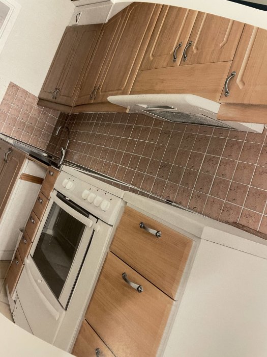 Kök före renovering med bruna kakelplattor och träskåp samt inbyggnadsugn och diskho.
