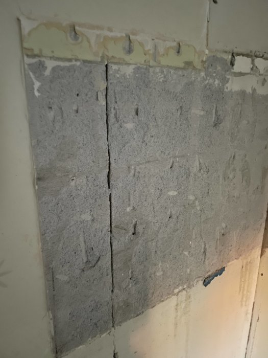Vägg med borttaget kakel och synligt spackel samt limrester i ett renoveringsprojekt.