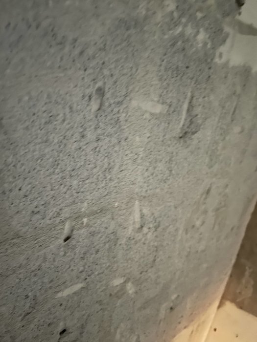 Närbild på en vägg där kakel har tagits bort, visande hårt material som eventuellt är spackel.