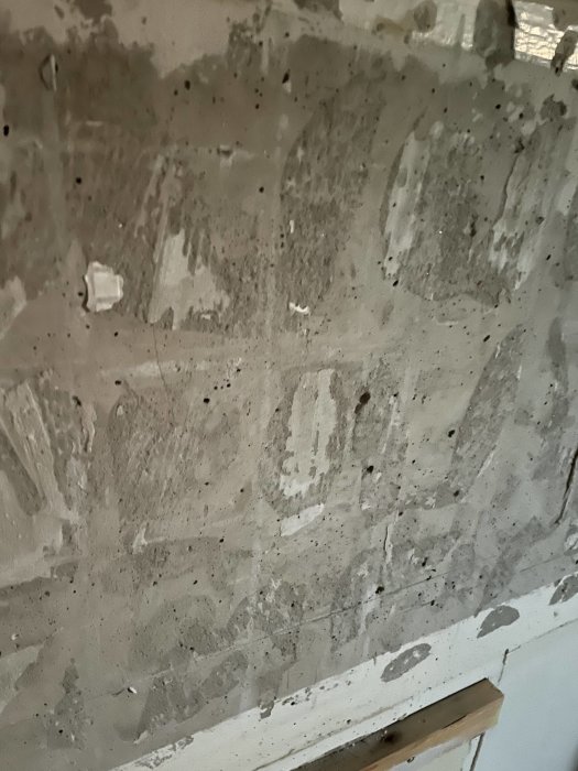 Vägg med avlägsnat kakel och exponerat spackel i ett renoveringsprojekt.