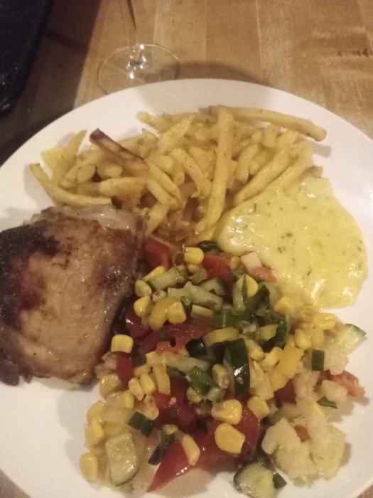 Grillad kycklingdel med pommes frites, blandad grönsallad och bearnaisesås på en vit tallrik.