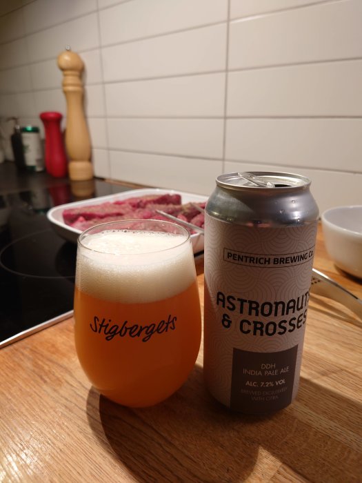 Ölglas fyllt med skummande dryck bredvid en ölburk märkt 'Astronaut & Crosses' på ett köksbord.