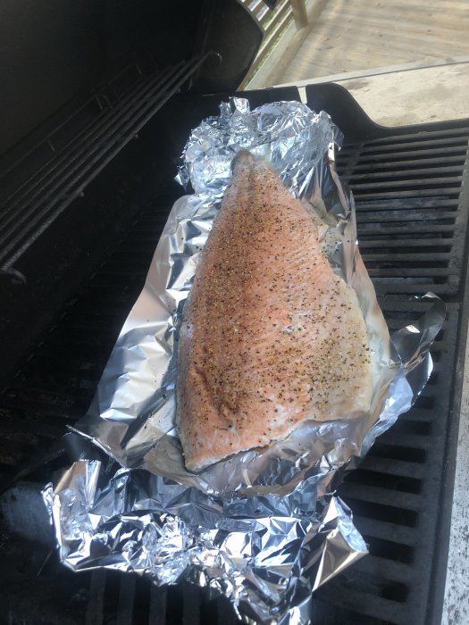 Kryddad laxfilé på folie i en grill, redo att grillas.