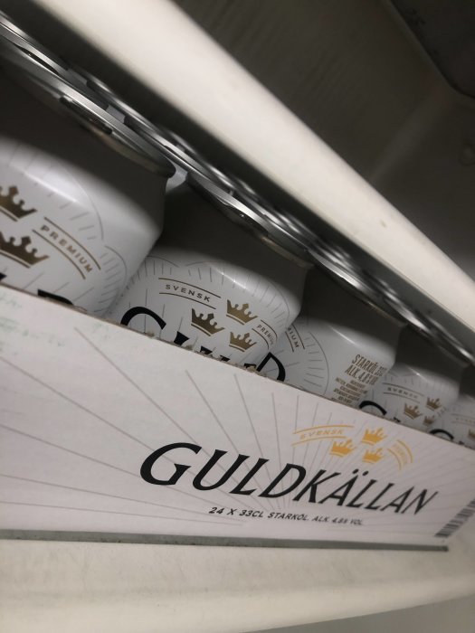 Flak med burkar av svensk öl märkt "Guldkällan" i ett kylskåp.