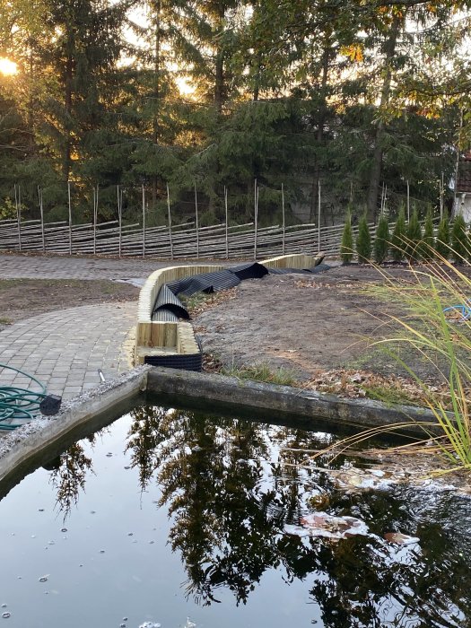 Halvfärdig bänk byggd som trappsteg upp till en gräsmatta med en damm i förgrunden.