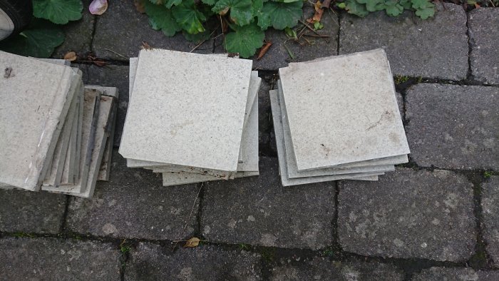 Staplar av gråmelerade golvklinker ligger på ett stenbelagt underlag, vissa smutsiga och använda.
