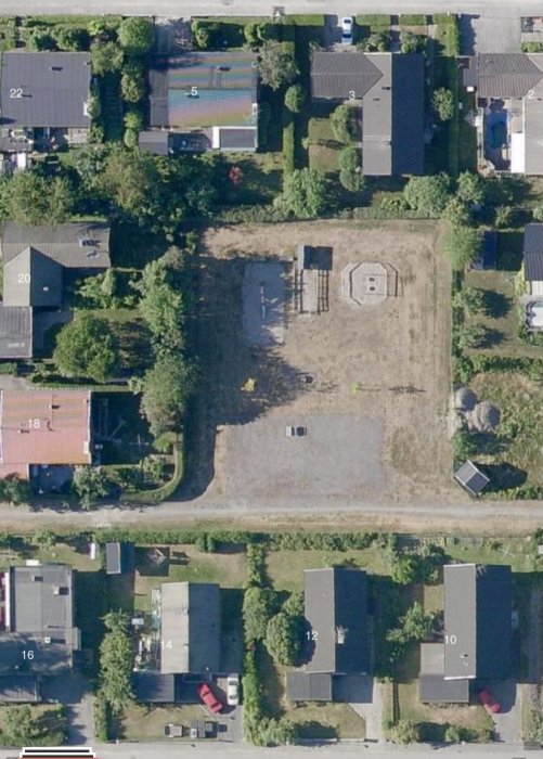 Flygbild över ett bostadsområde visande en lekplats med gulnande gräsmatta och sandiga ytor.