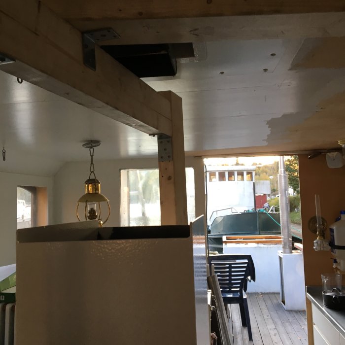 Inredning av båt med synlig träbjälke, installerad kamin och utsikt genom fönster mot annan båt.